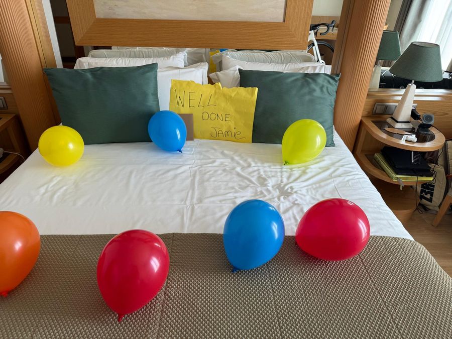 Hotel bed decorated with balloons and a Well Done Jamie sign