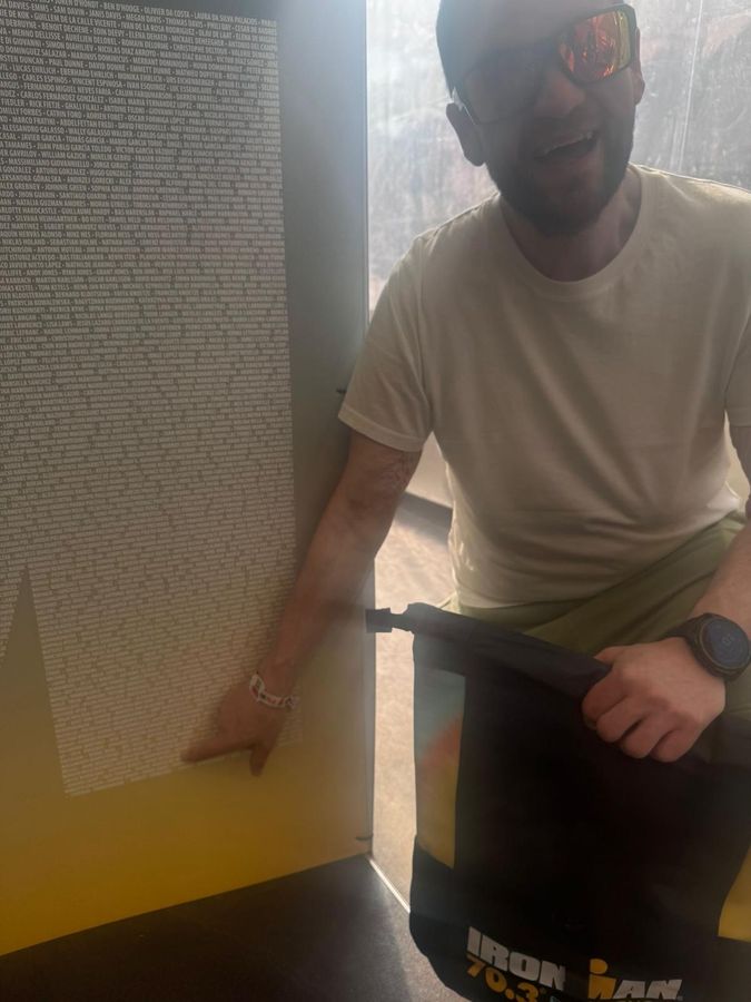 Jamie pointing at his name on the IRONMAN participant wall